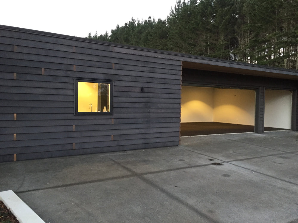 Timber house in Auckland with garage open showing freshly installed garage carpet with pine trees in the background