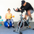 Man working out on a exercise bike on top of garage carpet and a lady on a Swiss ball with a dumb bell in her hand working out